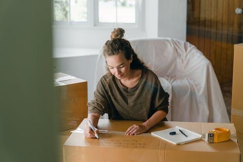 Free Woman signing box with marker while sitting in living room Stock Photo