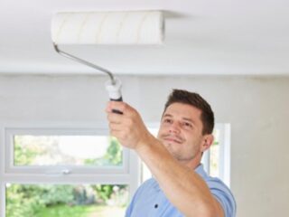 Man Painting Ceiling In Room Of House With Paint Roller